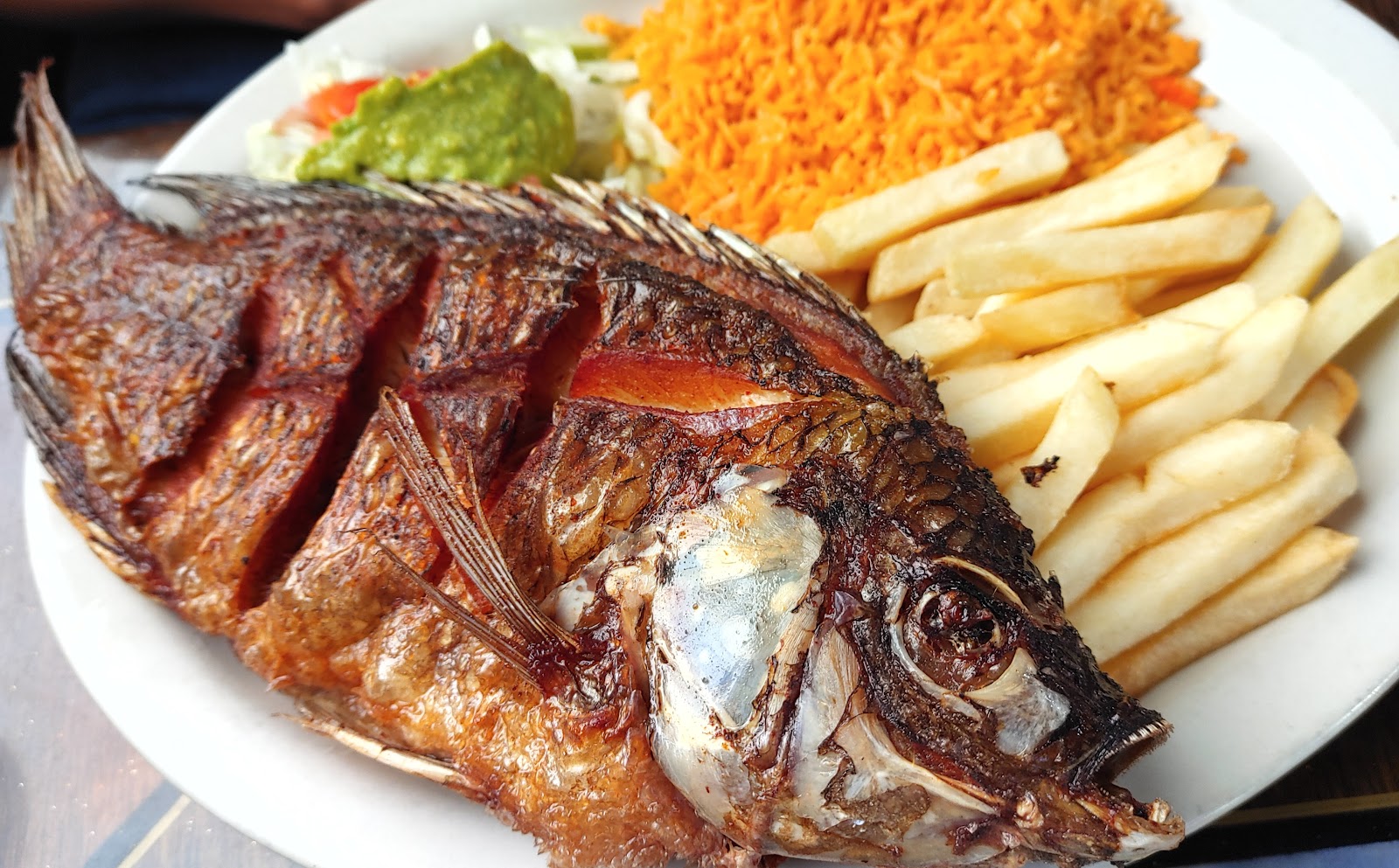 Whole fried mojarra fish with rice, fries and guacamole